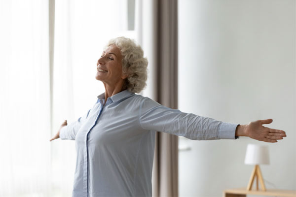 An older woman who has learned to breathe easier with COPD stretches her arms as she takes a deep breath.